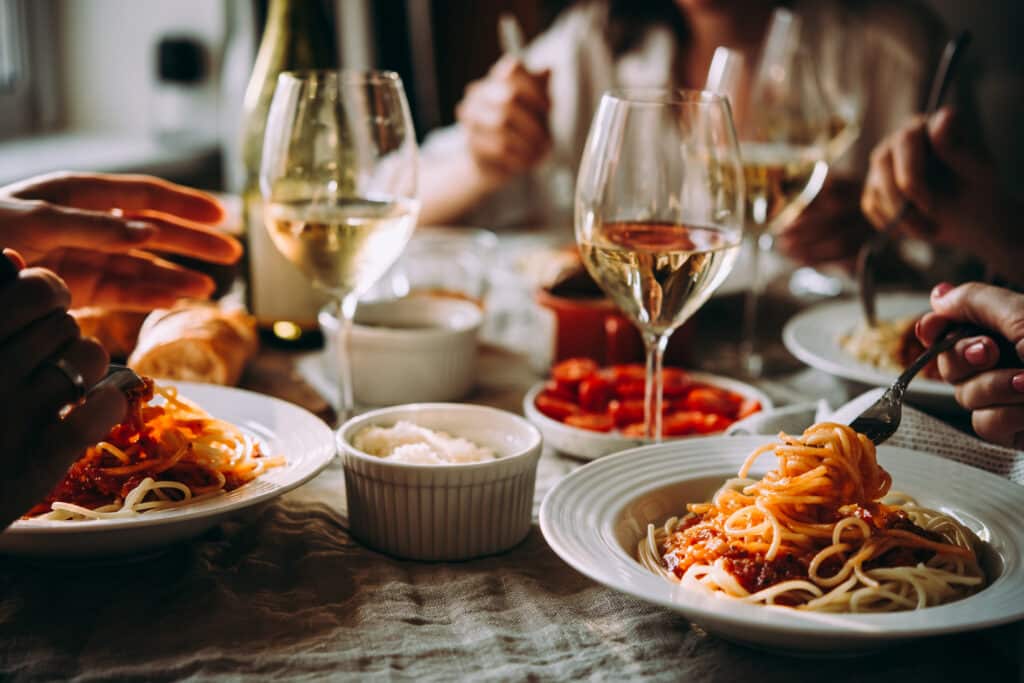 Mains twirlant des spaghettis à table, avec sauce tomate, vin blanc, parmesan, pain et tomates cerises. Dîner convivial.