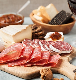 Délicieux plateau apéritif avec salami tranché, brie crémeux, confiture, crackers et vin rouge. Parfait pour une dégustation.