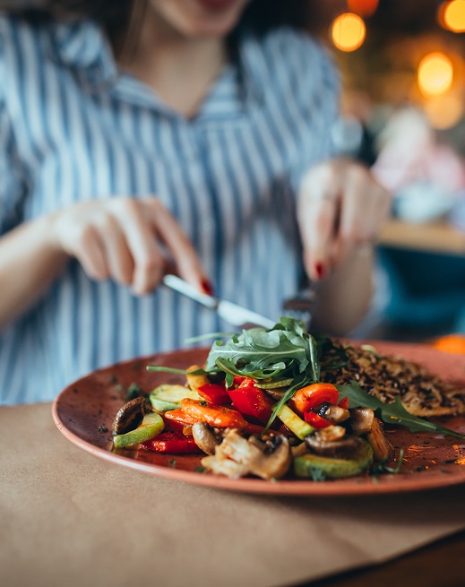 Femme en chemise rayée mange un plat végétarien sain avec légumes rôtis (champignons, poivrons, courgettes), roquette et riz.