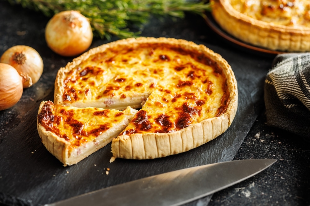 Quiche Lorraine Maison : Recette Traditionnelle Fondante Quiche Lorraine dorée sur une ardoise avec oignons et romarin, une part découpée prête à servir.