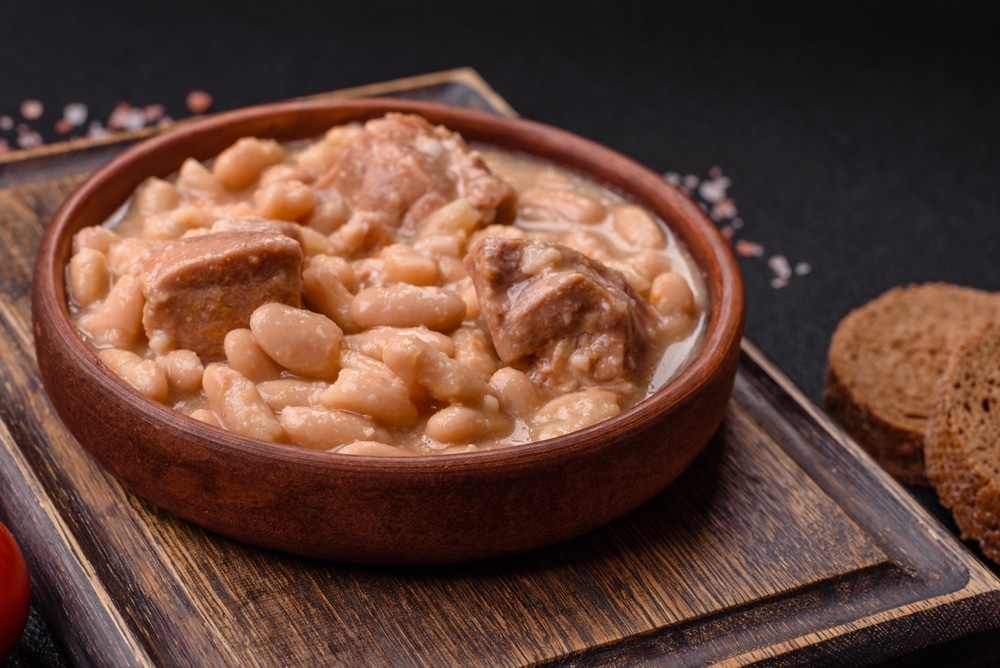 Ragoût de haricots blancs et viande : recette rustique Ragoût de haricots blancs et viande tendre dans un bol en terre cuite sur planche en bois rustique.